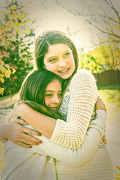 Two sisters hugging each other in a city park on a warm autumn day: Edmonton, Alberta, Canada