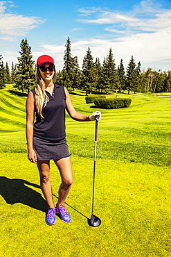 Portrait of a female golfer standing with her driver on the green grass of a golf club, Edmonton, Alberta, Canada