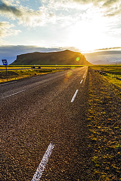 The sun sets behind the hills with a paved highway road leading into the sunset, Iceland