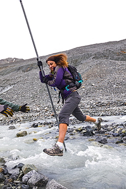 A woman jumps over a swift glacial stream with the aid of a pole near Gulkana Glacier, Alaska, United States of America