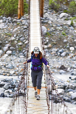 Female hiker crosses a wooden foot bridge on her way to Gulkana Glacier, Alaska, United States of America