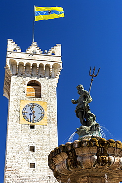 Fountain top of Poseidon with trident and large stone clock tower with flag of Trento in the background with blue sky, Trento, Trento, Italy