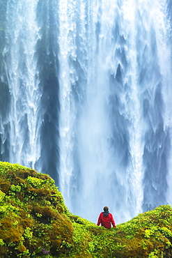 Man sitting on a mossy rock at base of Skogafoss waterfall, Iceland