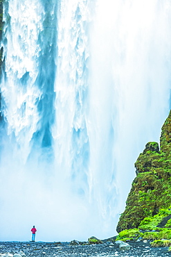 Man standing at base of Skogafoss waterfall, Iceland