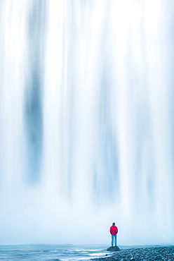 Man standing at base of Skogafoss waterfall, Iceland