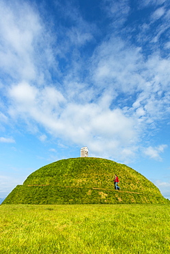 Man walking up Thufa grassy dome with fish drying house on top (art installation by Olof Nordal), Reykjavik, Iceland