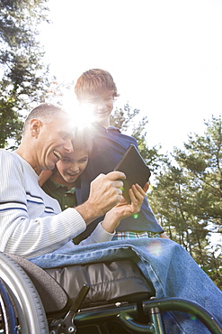 Man with spinal cord injury in wheelchair with his sons reading a tablet