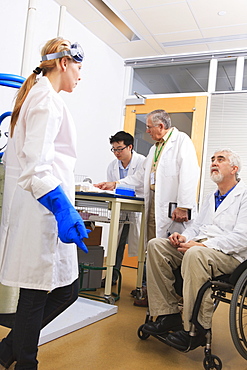 Professor with muscular dystrophy with engineering student and professor discussing log book for water distillation system in a laboratory