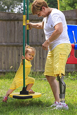 Grandmother with a prosthetic leg playing on a swing set with her granddaughter