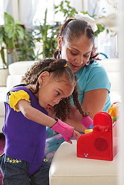 Mother helping small daughter with Cerebral Palsy play with a toy