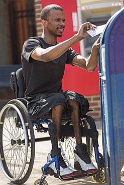 Man in a wheelchair who had Spinal Meningitis putting a letter in a public mail box