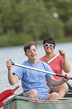 Young man with Down Syndrome rowing a canoe with his friend in a lake