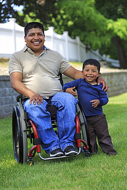 Portrait of Hispanic man with Spinal Cord Injury in wheelchair with his son in lawn