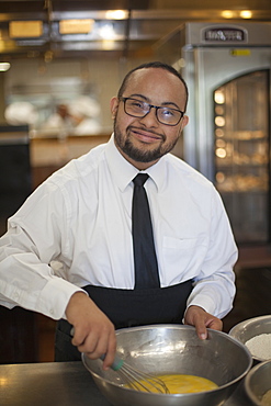 Happy African American man with Down Syndrome as a chef cooking in commercial kitchen