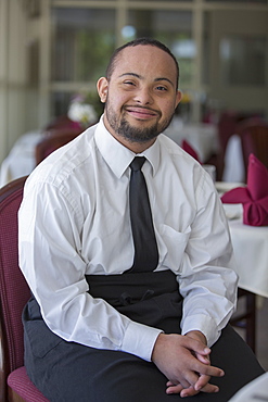 Portrait of happy African American man with Down Syndrome as a waiter in restaurant