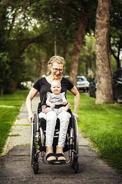 A paraplegic mom carrying her baby in her lap while using a wheelchair outdoors on a warm summer afternoon: Edmonton, Alberta, Canada