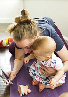 Mother showing image on smart phone to baby daughter; Vancouver, British Columbia, Canada