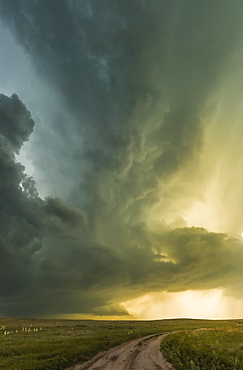 Supercell over the prairies and a dirt road, with sunlight illuminating the dramatic sky; Tulsa, Oklahoma, United States of America