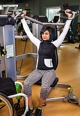 A paraplegic woman working out using an overhead press in a fitness facility; Sherwood Park, Alberta, Canada