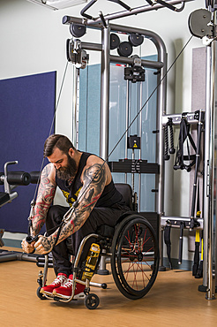 A paraplegic man working out using a crossover pulley weight lifting apparatus in a fitness facility; Sherwood Park, Alberta, Canada