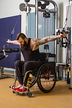 A paraplegic man working out using a crossover pulley weight lifting apparatus in a fitness facility; Sherwood Park, Alberta, Canada