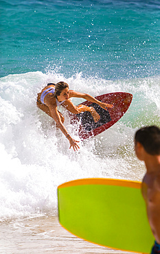 A young woman skimboarding on a wave off Sandy Beach, Oahu; Oahu, Hawaii, United States of America