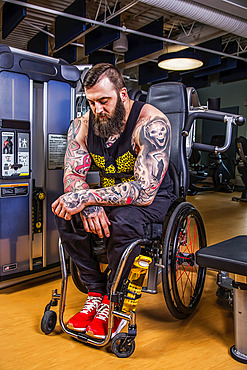 A paraplegic man resting after working out using an overhead press in fitness facility; Sherwood Park, Alberta, Canada