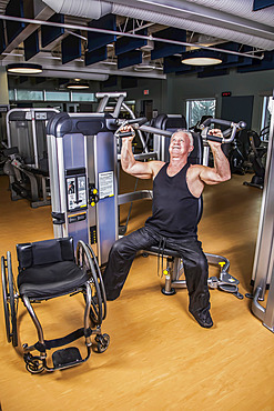 An older paraplegic man working out using an overhead press in fitness facility; Sherwood Park, Alberta, Canada