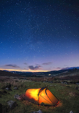 A lit up tent pitched in the Wicklow Mountains at night with stars in the sky; County Wicklow, Ireland