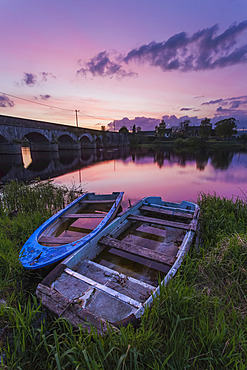 Two old wooden boats on the banks of the Shannon River at sunset with a stone bridge in the background; Montpellier, County Limerick, Ireland