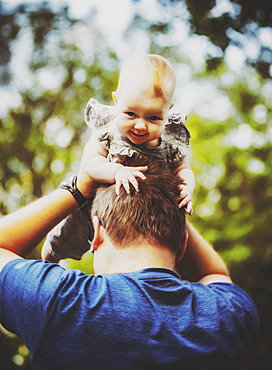 A father holding his baby girl in the air while outdoors during the fall; Edmonton, Alberta, Canada