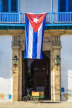 The national flag of Cuba hangs over the entrance to the Palace of the Artisans (Palacio de la Artesania), Old Town; Havana, Cuba