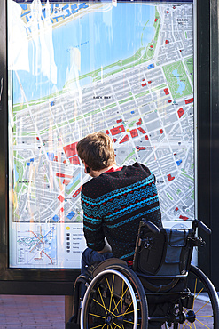 Man in a wheelchair looking at a map of a city posted on a wall