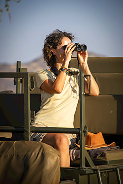 Woman sitting in sunlit jeep using binoculars on safari at the Gabus Game Ranch; Otavi, Otjozondjupa, Namibia