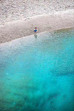 The Blue Pools of Makarora offer enticing blue waters to swim in. A woman crouches by the water's edge to take a picture with her camera, Mount Aspiring National Park; Makarora, Otago, New Zealand