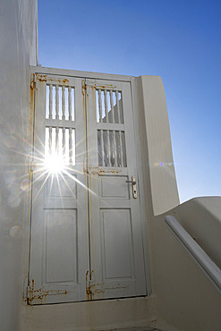 Sunburst shines through a door on a whitewash building with blue sky on the island of Mykonos, Mykonos, South Aegean, Greece