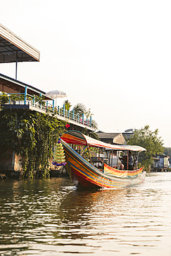 Traditional boat in colourful stripes travels along a river in Asia