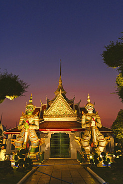 Wat Arun Ratchawararam Ratchawaramahawihan with Yaksha Guardian Statues at the entrance to Ordination Hall, illuminated at dusk, Bangkok, Bangkok Yai District, Thailand