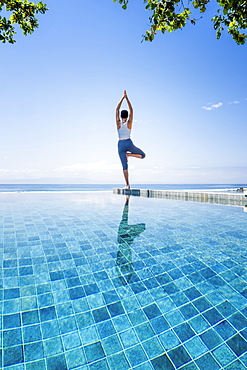 A young woman practising yoga next to an infinity pool, Candidasa, Bali, Indonesia, Southeast Asia, Asia