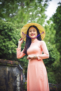 Portrait of a young Vietnamese woman in an Ao Dai dress and conical hat at a Buddhist temple, Hue, Vietnam, Indochina, Southeast Asia, Asia