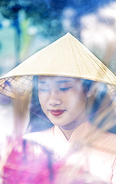 A young Vietnamese woman in a conical hat making incense offerings at a Buddhist temple, Hue, Vietnam, Indochina, Southeast Asia, Asia