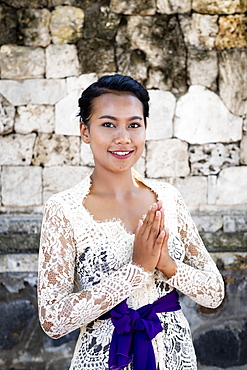 A young Balinese woman in a local temple dress making a formal greeting and smiling, Bali, Indonesia, Southeast Asia, Asia