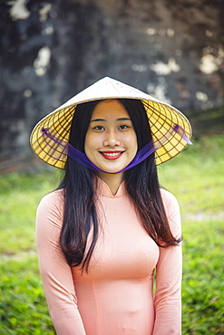 A young Vietnamese woman in a traditional Ao Dai dress and conical hat and smiling, Hue, Vietnam, Indochina, Southeast Asia, Asia