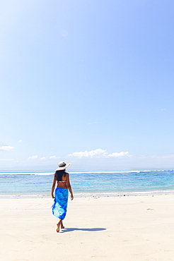 A young woman in a sunhat and shawl walking along a pristine tropical beach on Bali island, Indonesia, Southeast Asia, Asia