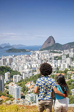 A multi-ethnic couple arm in arm looking out over Sugar Loaf mountain and the Rio skyline, Rio de Janeiro, Brazil, South America