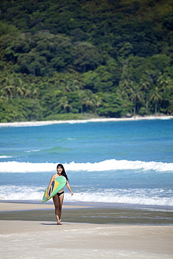 Beach shot of a Japanese Brazilian (Nipo-brasileiro) in a bikini carrying a surf board decorated with the Brazilian flag, Brazil, South America