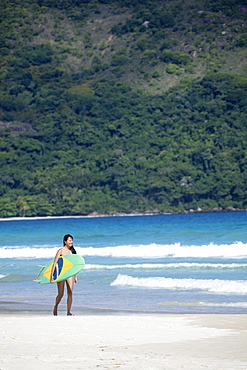 Beach shot of a Japanese Brazilian (Nipo-brasileiro) in a bikini carrying a surf board decorated with the Brazilian flag, Brazil, South America