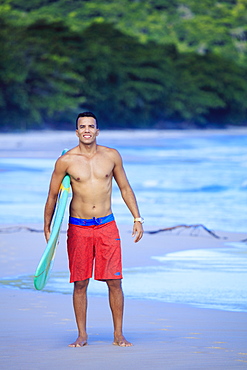 Brazilian male surfer with a Brazilian flag surfboard on a beach in Rio de Janeiro state, Brazil, South America