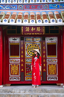 A young Vietnamese woman wearing a traditional Ao Dai dress and standing outside a temple in the historic town centre, Hoi An, Vietnam, Indochina, Southeast Asia, Asia