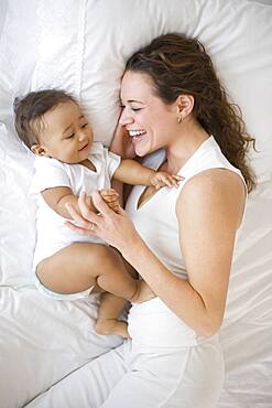 Hispanic mother playing with baby on bed